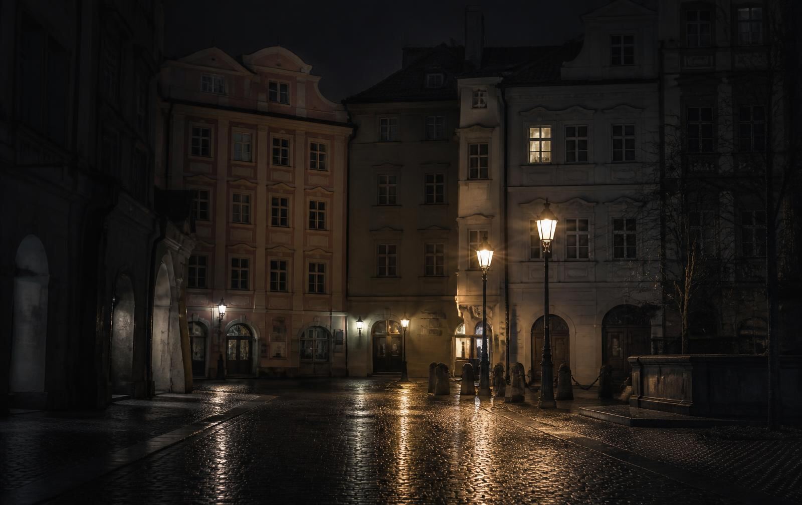 Rain-wet street in a Polish city at night, brick and stone facades in deep shadow, warm lamplight on the cobbles and a single lit upper window
