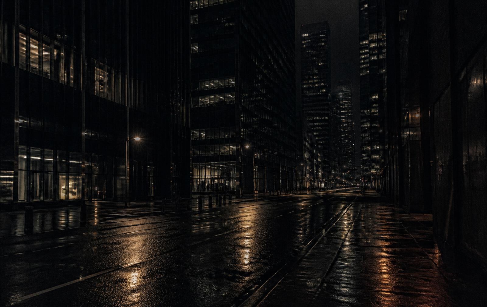 An empty financial district street after rain at night, glass towers with scattered lit windows reflected on wet asphalt