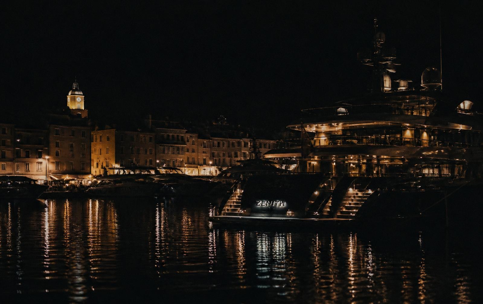 Saint-Tropez harbour at midnight with yacht lights reflected on dark water and lit old town facades