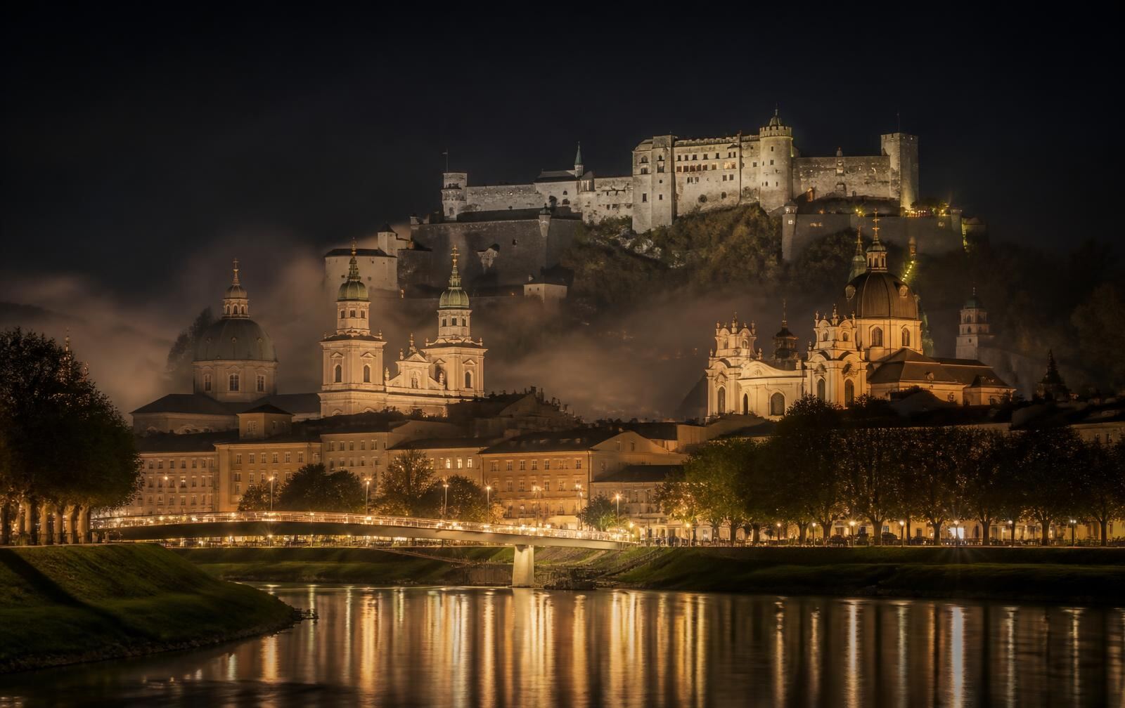 Salzburg baroque domes and hilltop fortress glowing gold above the river in evening mist