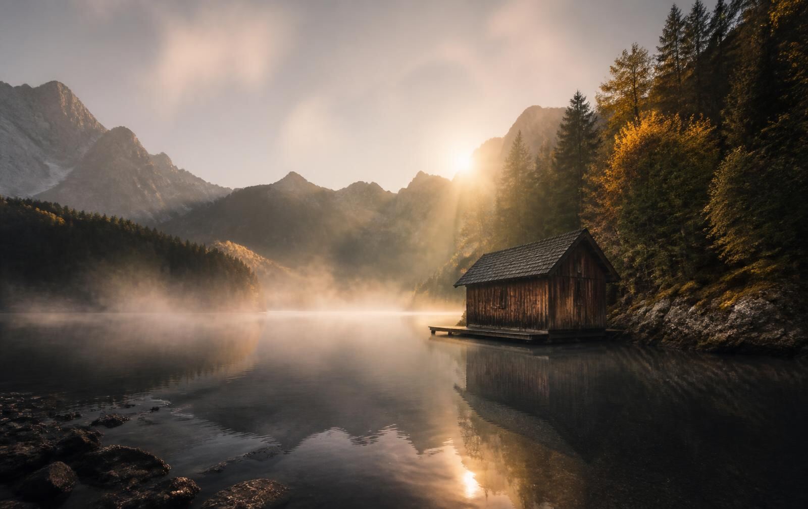 A misty Austrian lake at dawn with a wooden boathouse and forested mountain slopes behind