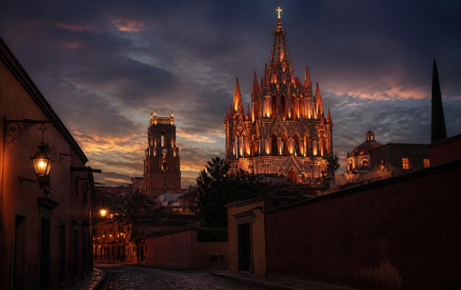 The pink spire of San Miguel de Allende's parish church lit at dusk above a cobbled street with lanterns