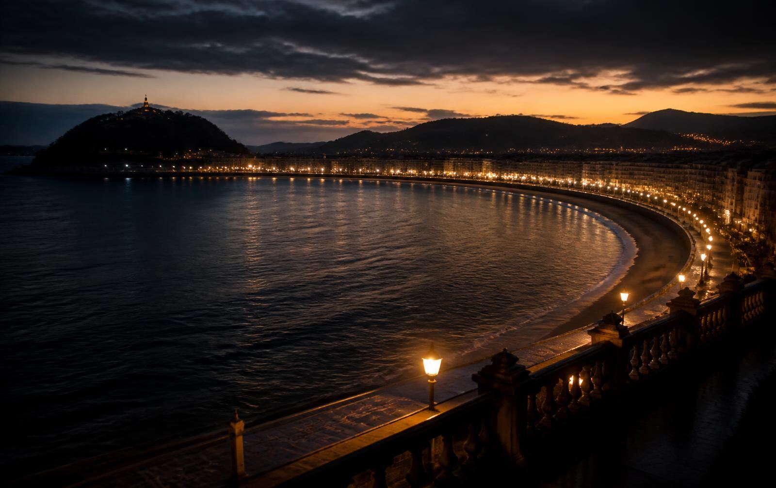 The curving bay of San Sebastián at dusk with a lamplit promenade above dark Atlantic water