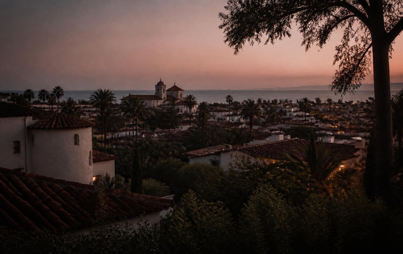 Santa Barbara waterfront at dusk with a private terrace lit warmly above the Pacific