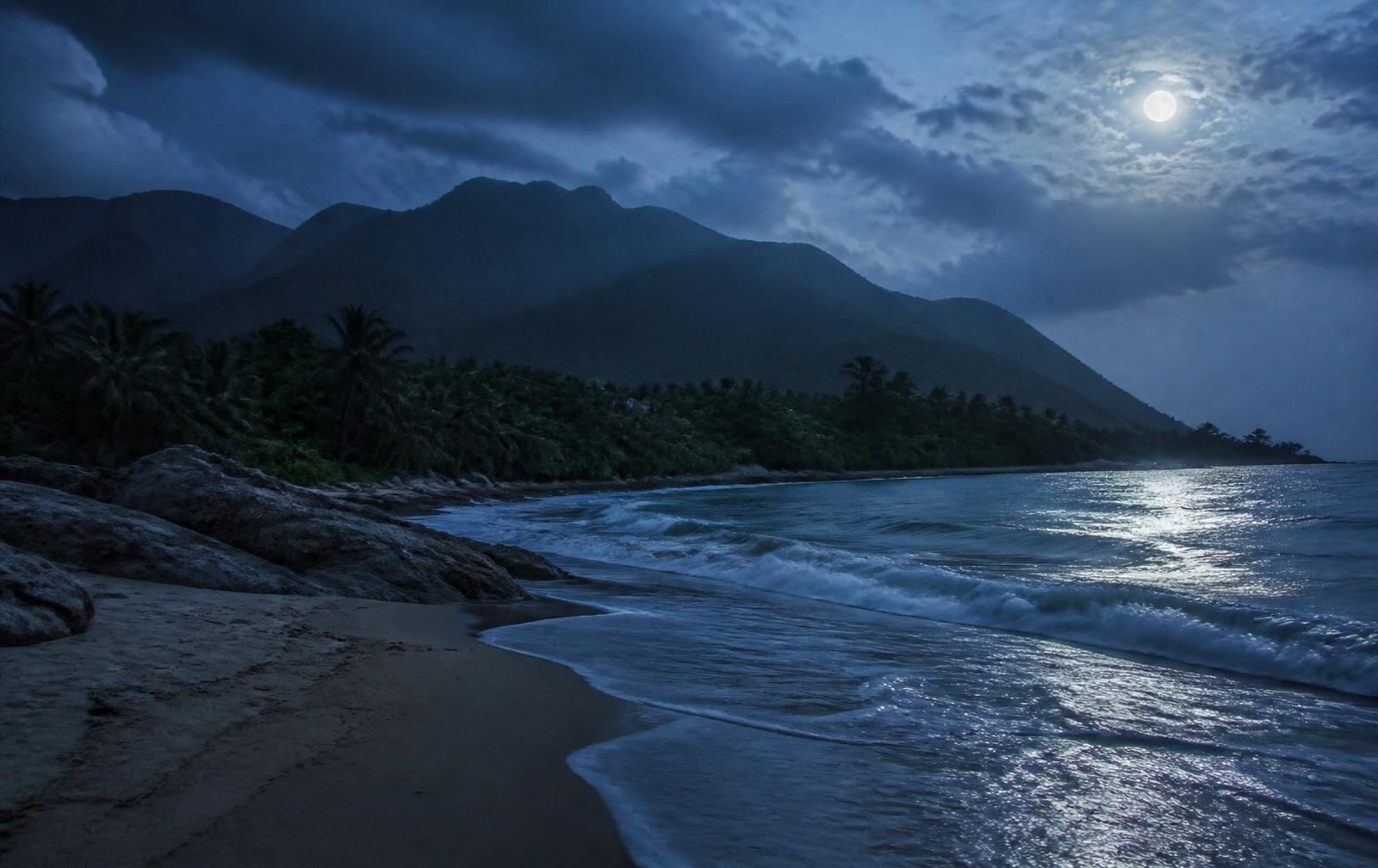 Moonlit Caribbean beach near Santa Marta with Sierra Nevada mountain silhouettes behind the jungle