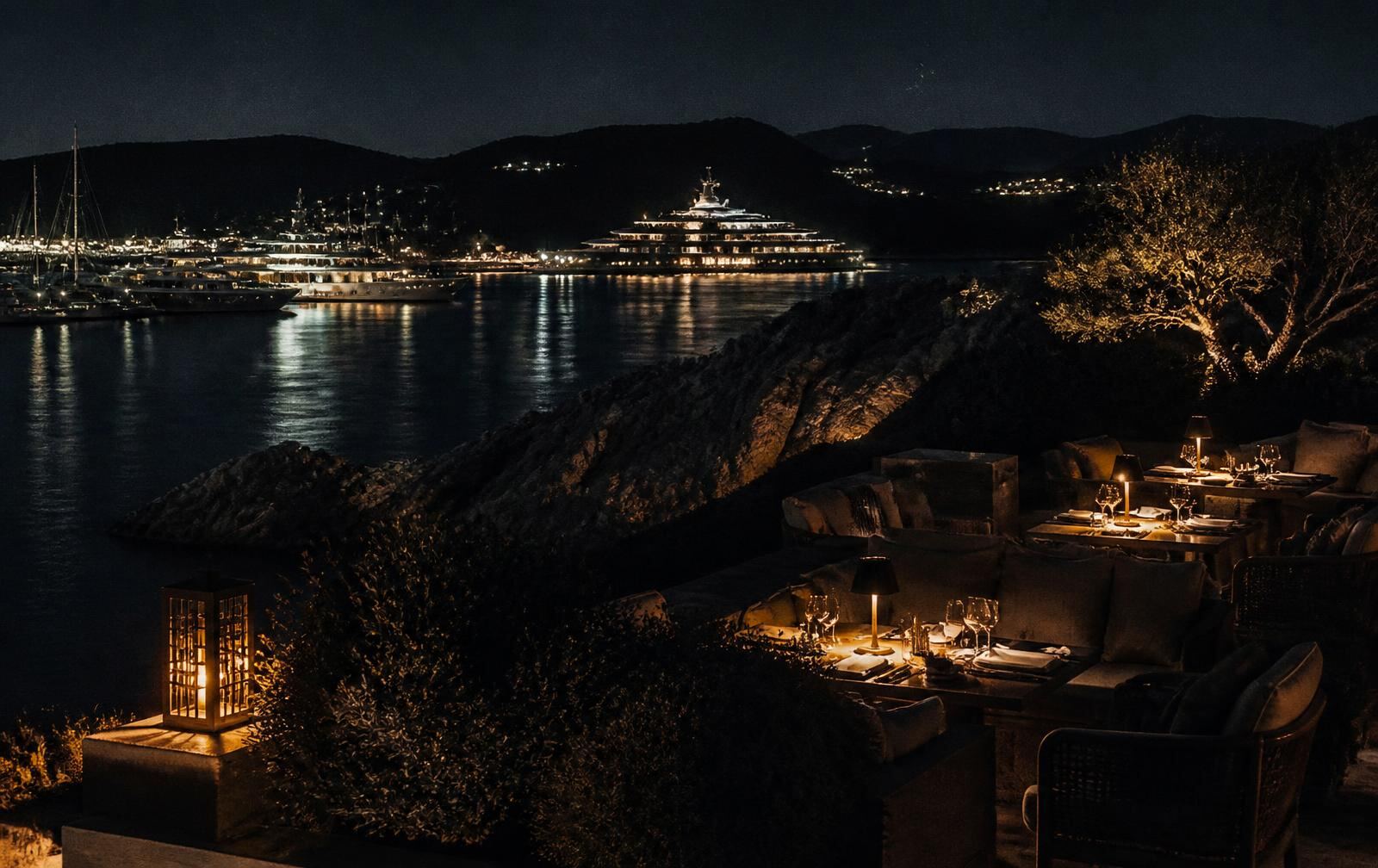 A lantern-lit terrace above a dark Sardinian bay with yachts illuminated in the marina beyond