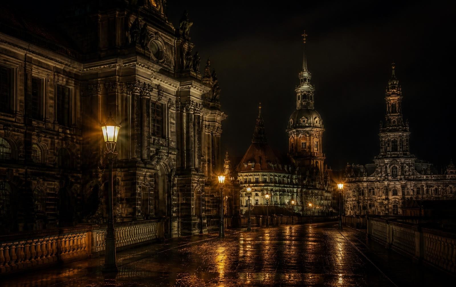 Ornate baroque stone facades in Saxony at night with lantern light reflected on wet cobbles