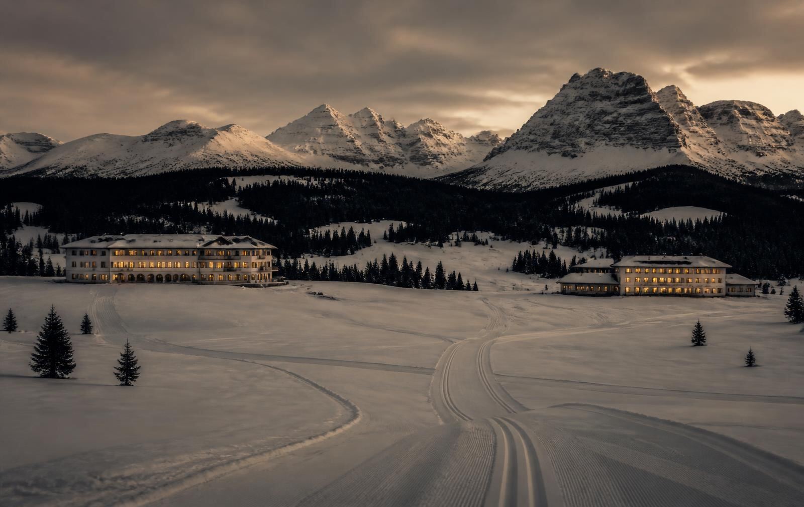A snow-covered alpine plateau at dusk with elegant low hotels lit warm gold and dark peaks beyond
