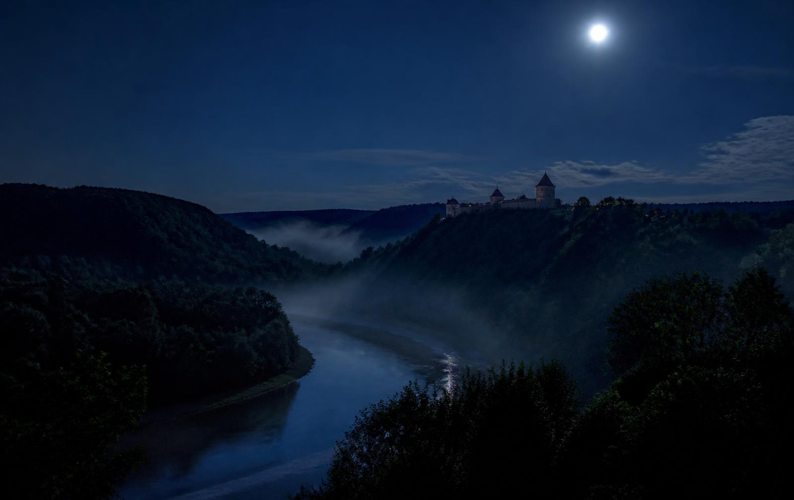 The Gauja river valley at night — mist over dark forest, a moonlit castle silhouette on a distant ridge