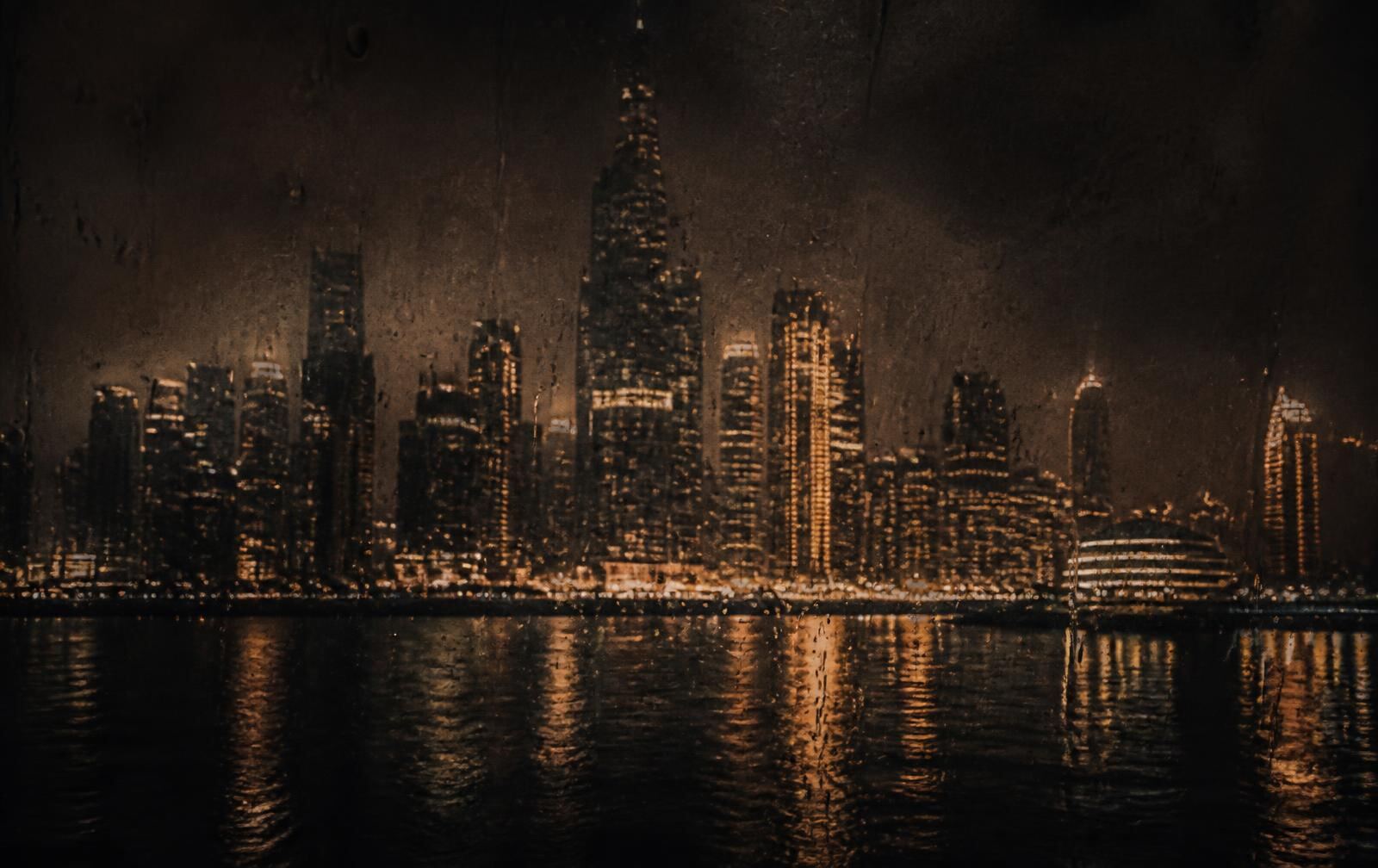 A tropical city skyline at night seen through rain-streaked glass, warm gold towers reflected on dark water