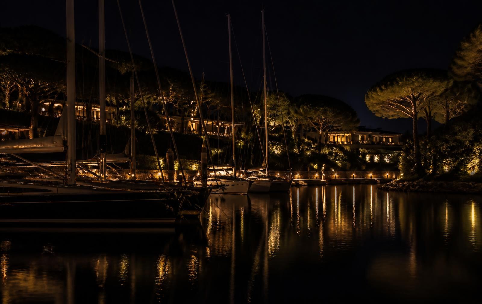A quiet Sotogrande marina at night with moored sailing yachts and warm gold dock lamps on still water