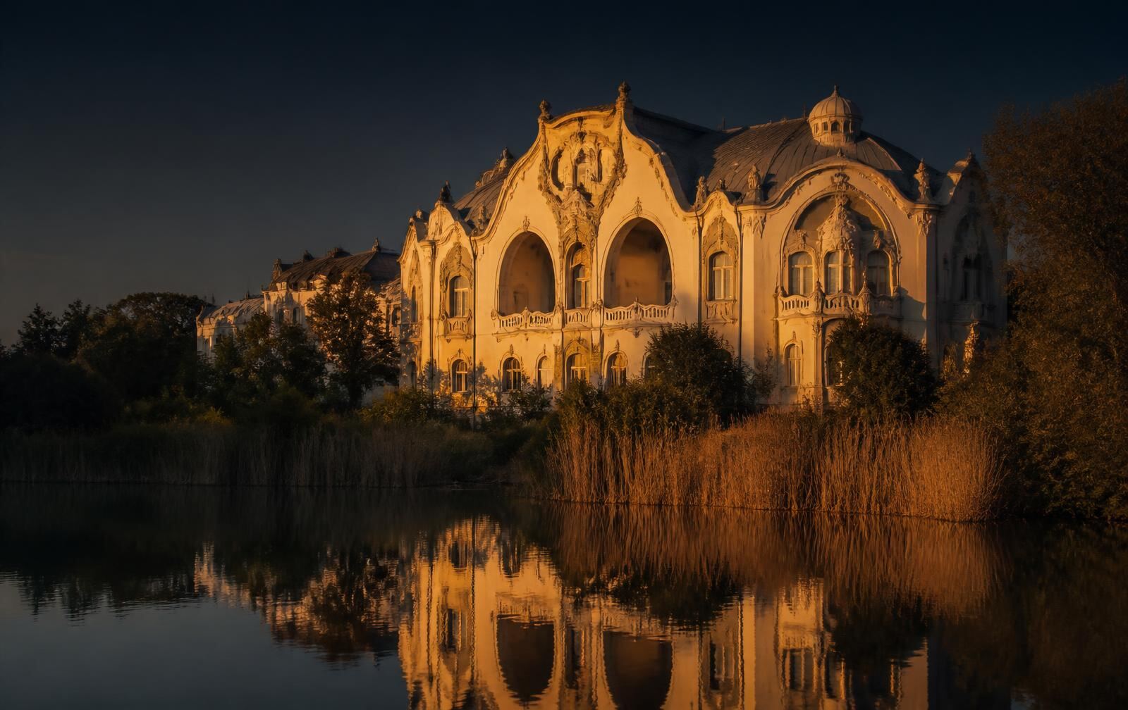 An ornate art nouveau pavilion beside a calm reed-fringed lake in warm gold evening light