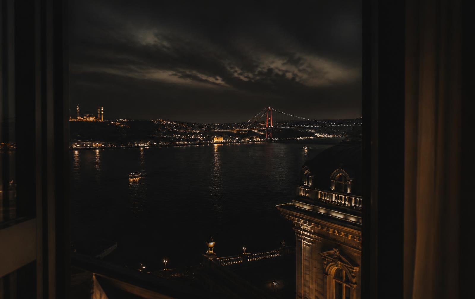 The Bosphorus at night seen from a high window, dark water with scattered warm city lights