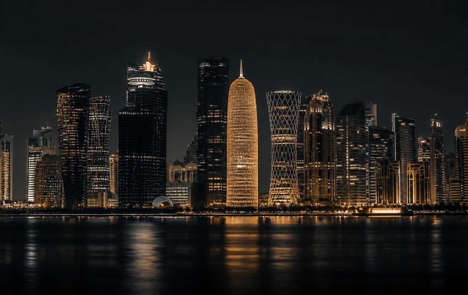 A modern Gulf skyline at night seen across dark calm water with warm gold tower lights