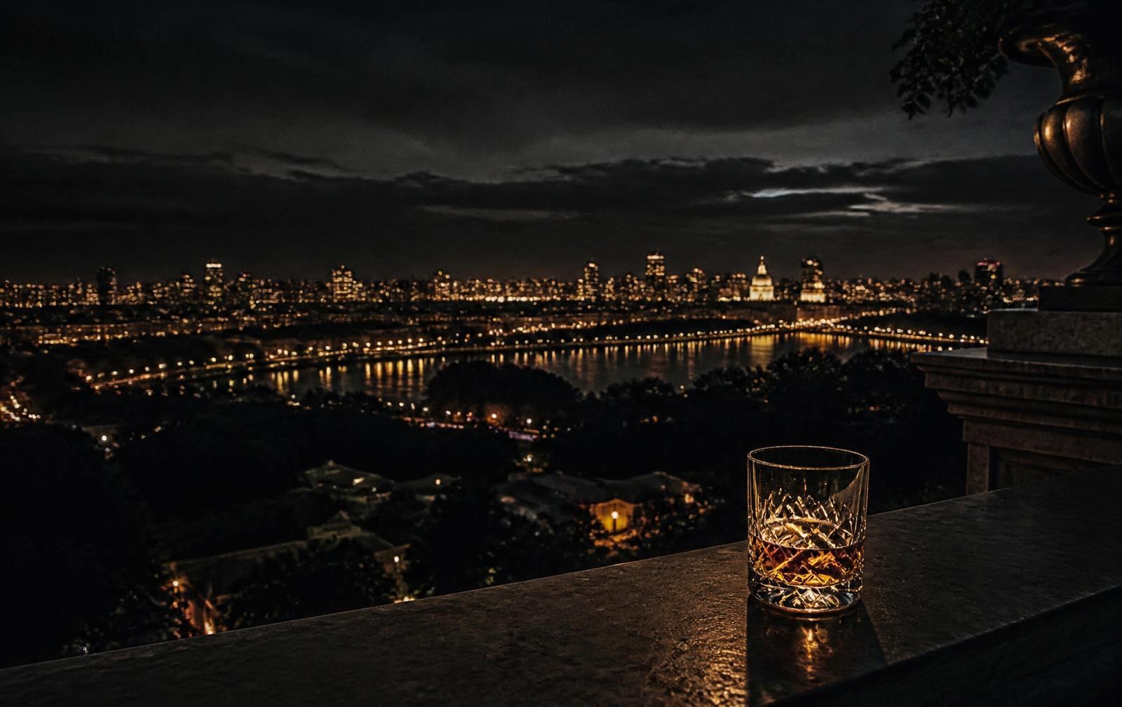 Distant American city lights at night seen from a dark private terrace with a single glass on the stone ledge
