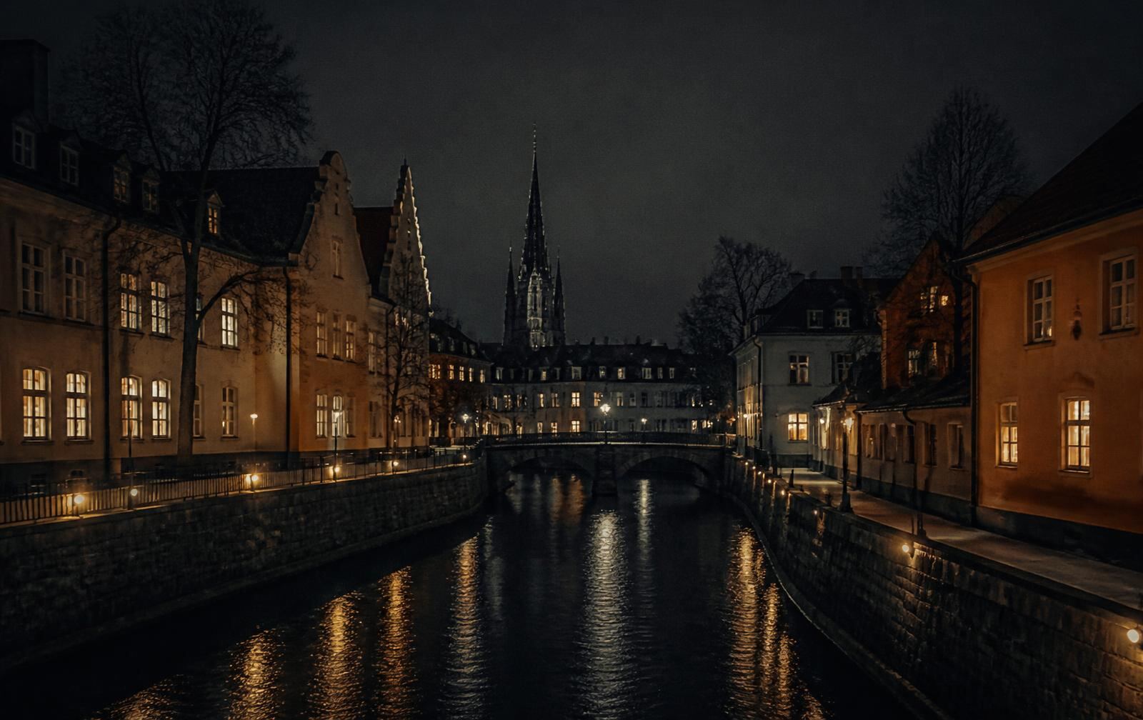 A small historic Swedish city at night, a narrow river between stone embankments with warm lit windows and a cathedral spire in the dark distance