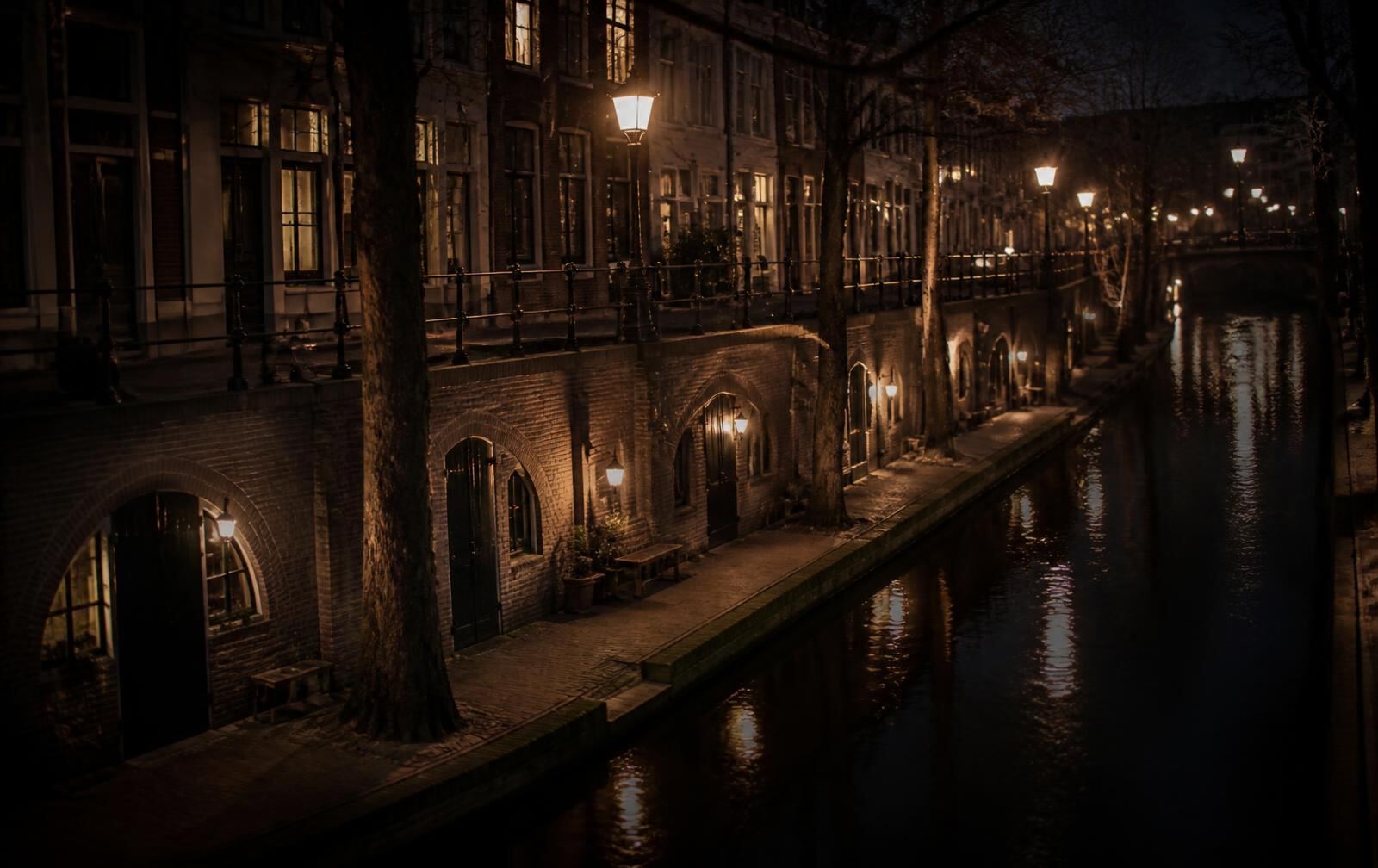 Utrecht canal at night with its lower stone wharf, brick cellar archways along the waterside and warm lamplight