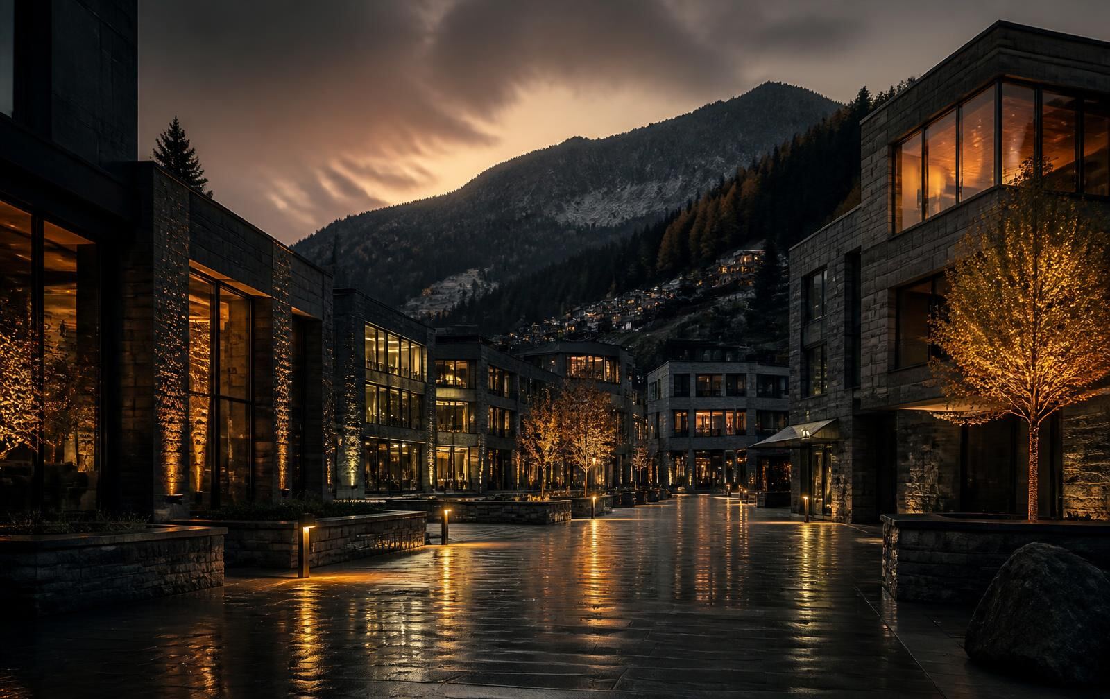 Vaduz at dusk with low stone and glass buildings, warm lit windows and a wooded mountain ridge behind