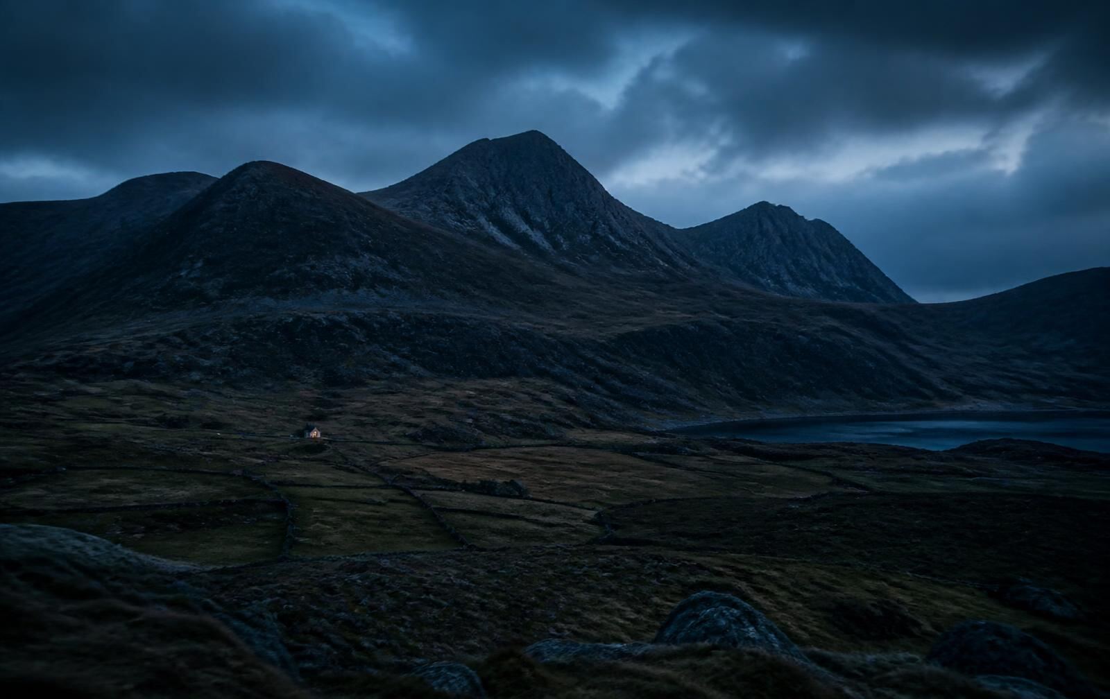 Welsh mountains at blue hour above a dark valley with a single distant lit cottage