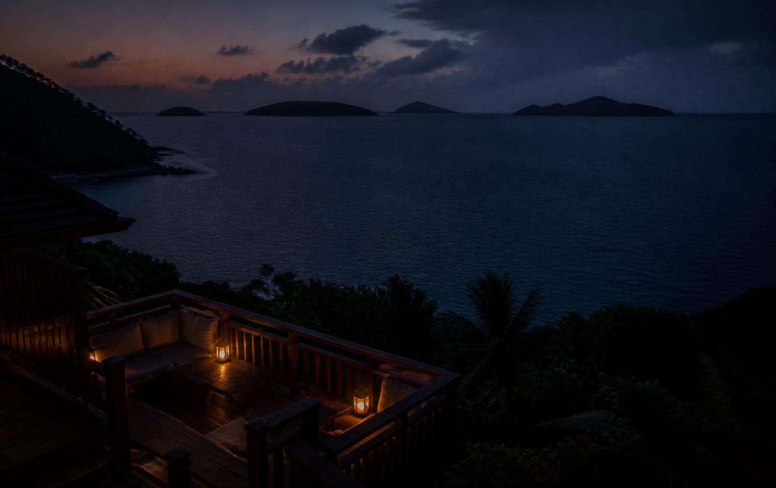 Tropical islands on a dark ocean horizon at late dusk seen from a lantern-lit timber terrace