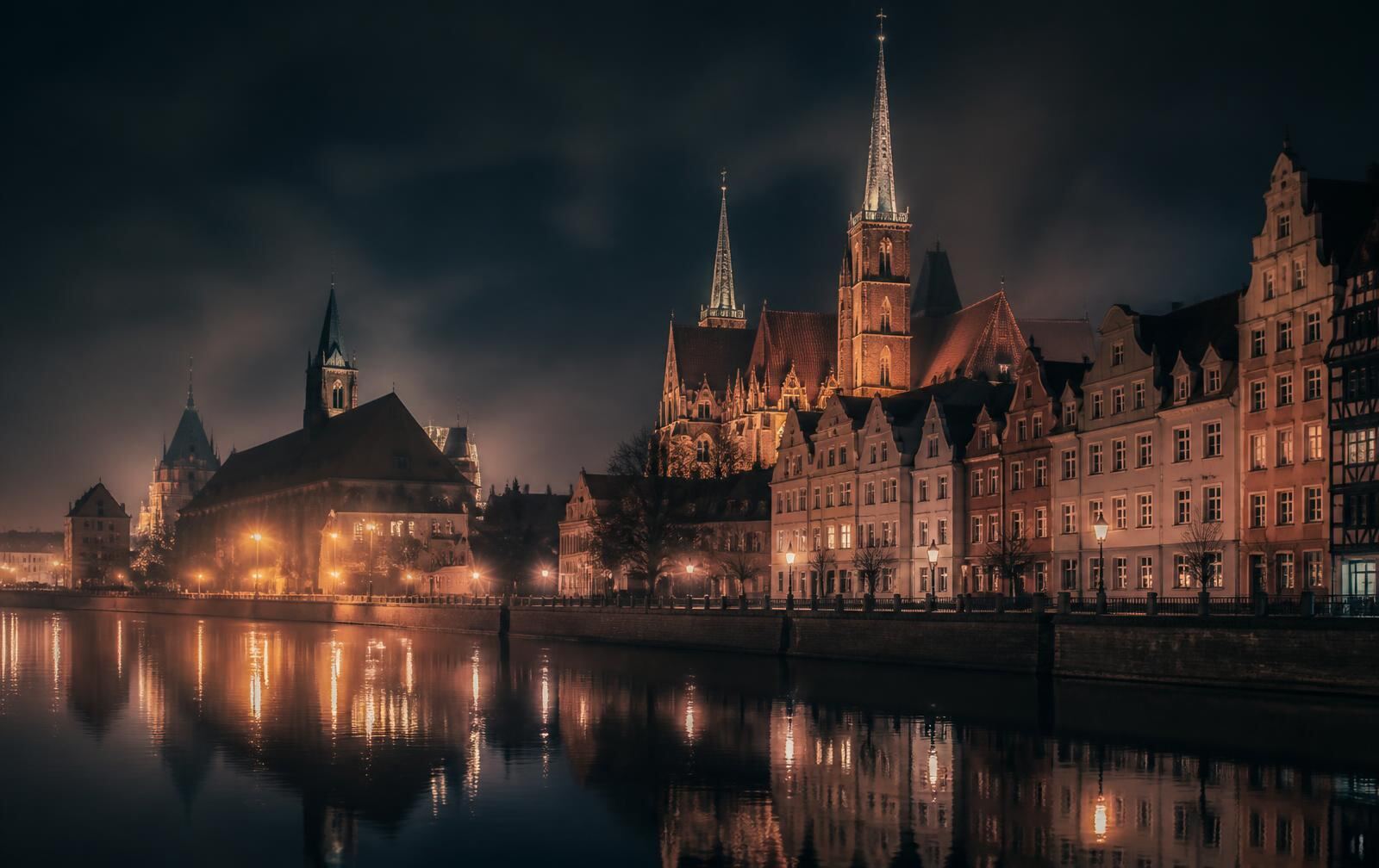 Wrocław market square at night, tall colourful gabled townhouses lit from within, wet cobblestones and an empty square under a dark sky